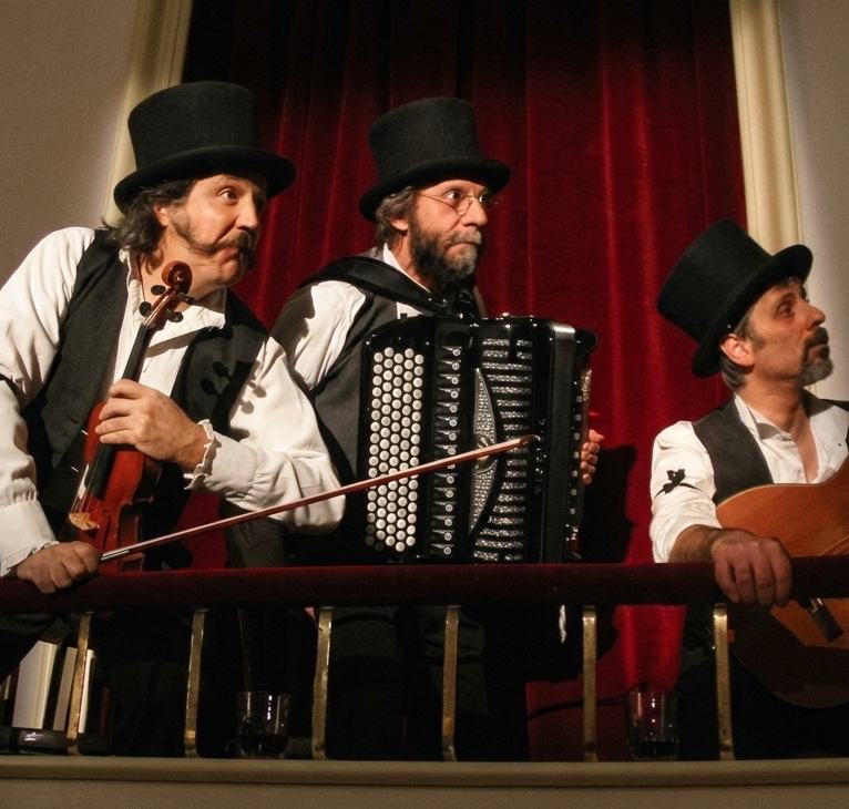 Tre musicisti in cilindro, violino e fisarmonica, davanti a un sipario rosso, foto 8 di 8
